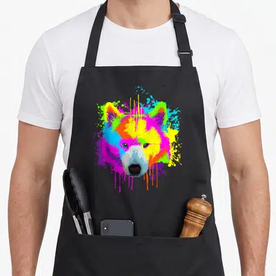 Splash samoyed dog apron - Cartoon dog head with yellow pink blue green purple paint splatters and drips — shown on a black cotton canvas apron against a white background