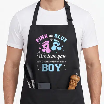 But apron or apron - PINK OR BLUE text with pink and blue baby footprints and hearts — shown on a black cotton canvas apron against a white background