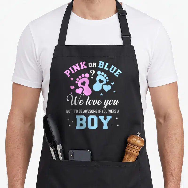 But apron or apron - PINK OR BLUE text with pink and blue baby footprints and hearts — shown on a black cotton canvas apron against a white background