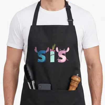 Sis sister family aprons - Cartoon SIS text with blue ears, pink bow, yellow straws, and pink ears — shown on a black cotton canvas apron against a white background