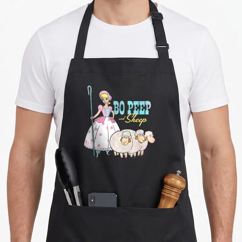 Funny peep sheep apron - Bo Peep holding a crook beside three sheep with blue and yellow text — shown on a black cotton canvas apron against a white background