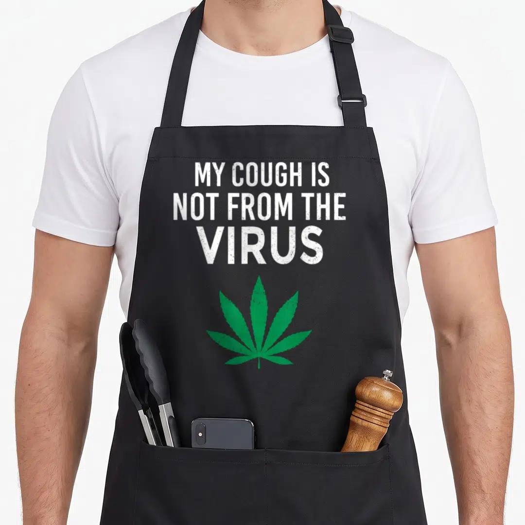 Cough smoker apron - White distressed text MY COUGH IS NOT FROM THE VIRUS above a green cannabis leaf — shown on a black cotton canvas apron against a white background