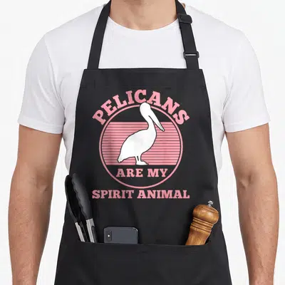 Cute pelican apron - White pelican inside pink striped circle with arched text above and straight text below — shown on a black cotton canvas apron against a white background