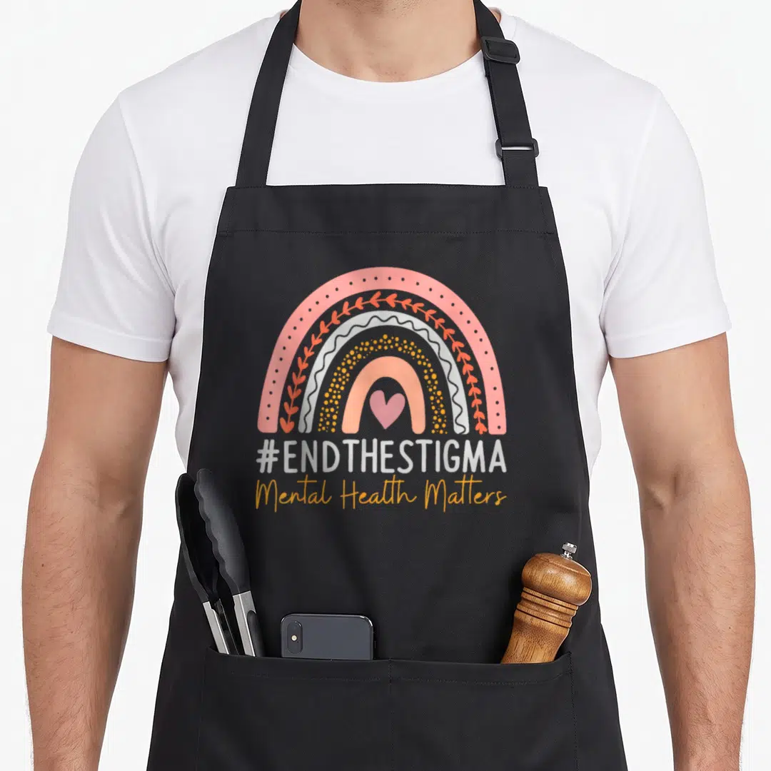 Health boho apron - Rainbow with pink heart and #ENDTHESTIGMA Mental Health Matters text — shown on a black cotton canvas apron against a white background