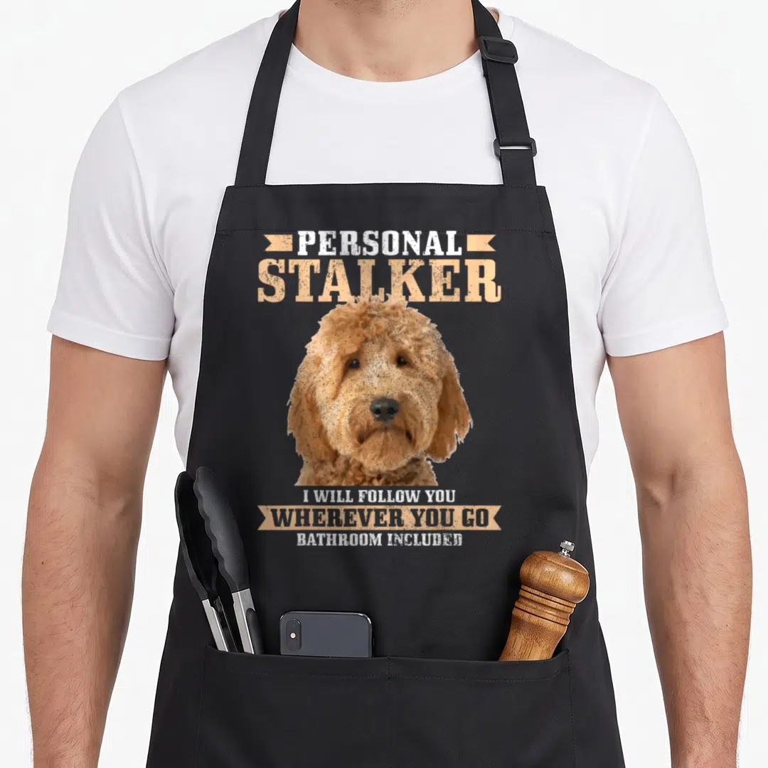 Goldendoodle personal chef apron - Personal stalker text above tan distressed dog head with ribbon banners — shown on a black cotton canvas apron against a white background