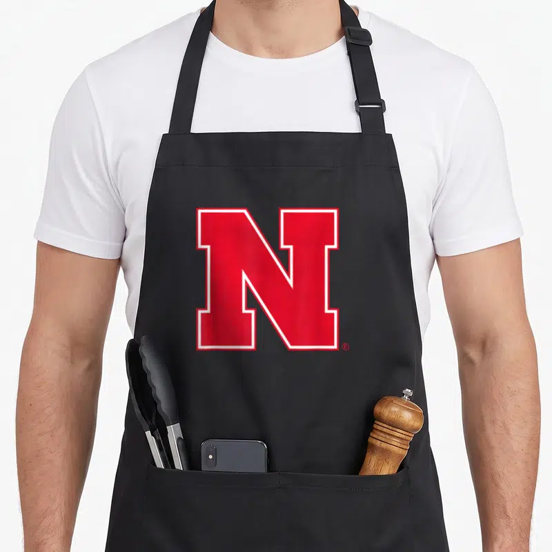 Icon nebraska boy apron - Large red N with white border on grey background — shown on a black cotton canvas apron against a white background