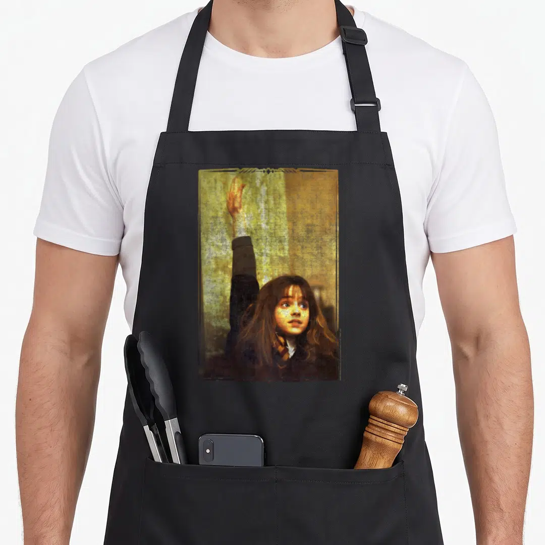 Granger novelty apron - Photo of a girl with brown hair raising her right arm inside a gold frame — shown on a black cotton canvas apron against a white background