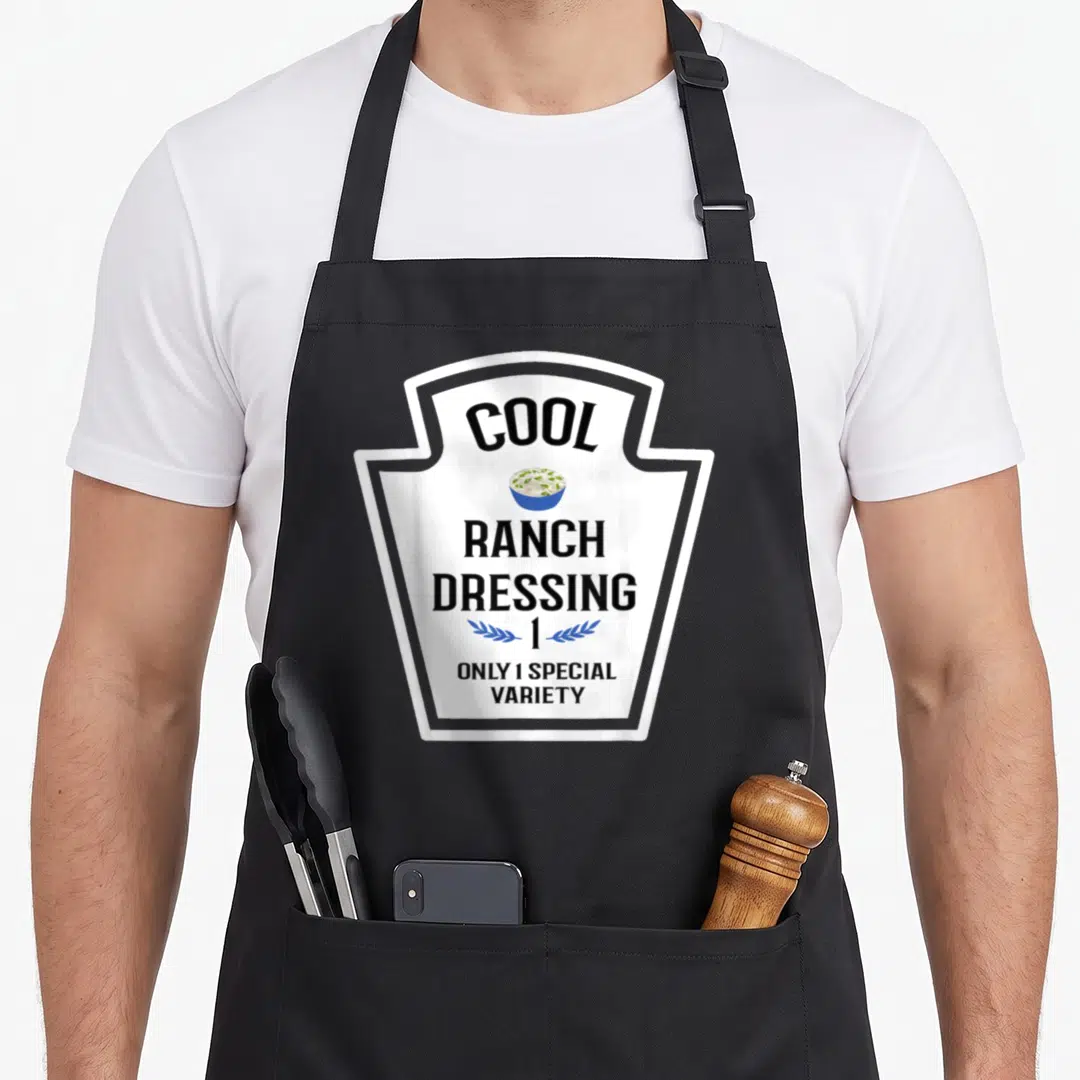 Dressing family aprons - Shield graphic with Cool Ranch Dressing text, blue bowl, and number 1 laurel wreath — shown on a black cotton canvas apron against a white background