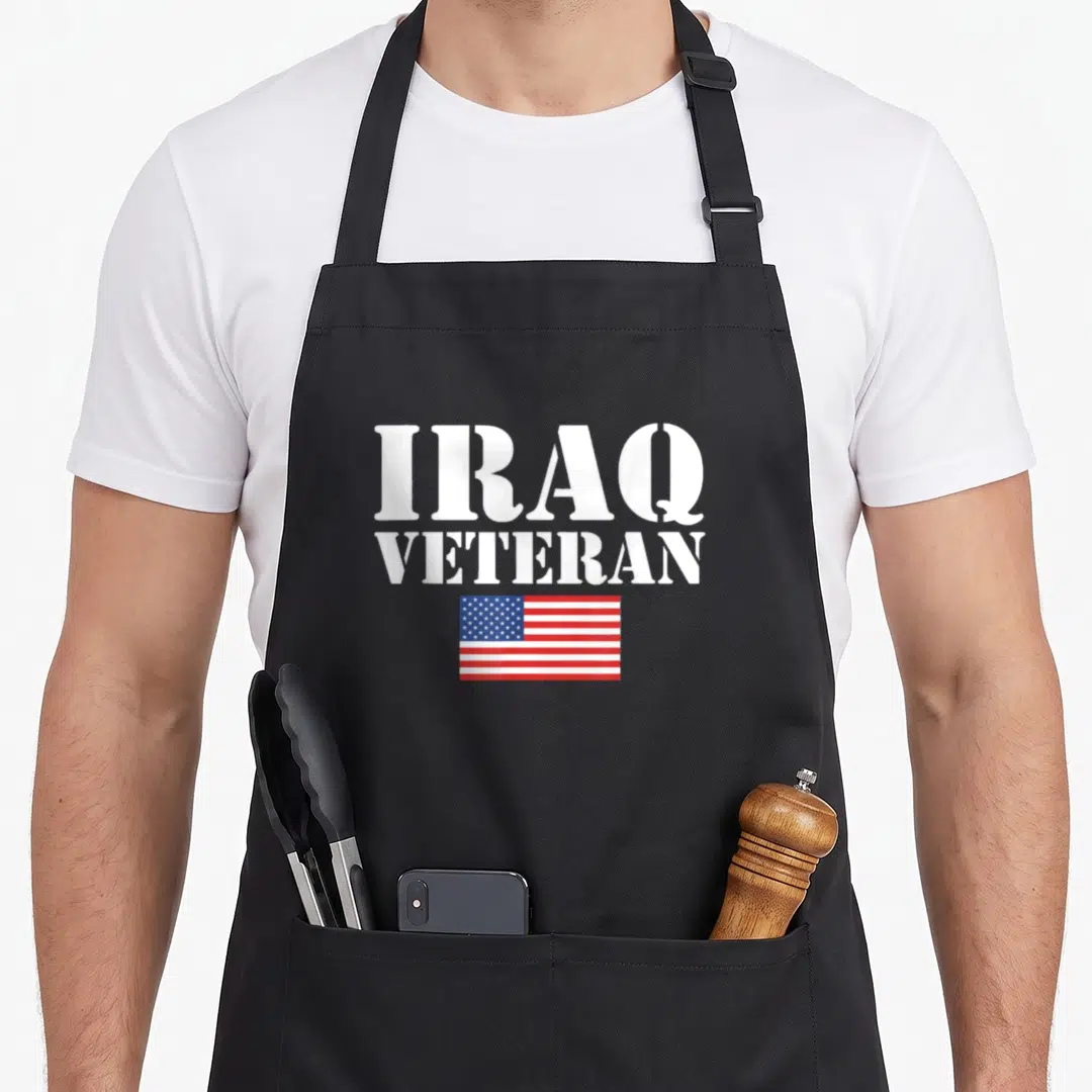Iraq patriots apron - Stacked white text IRAQ VETERAN above a red white blue USA flag — shown on a black cotton canvas apron against a white background