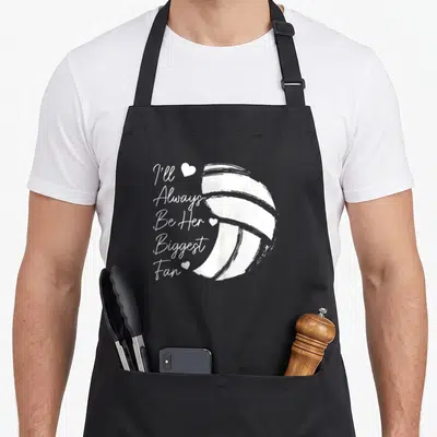 Volleyball mom daughter apron - White stacked text I'll Always Be Her Biggest Fan next to a large volleyball and three — shown on a black cotton canvas apron against a white background