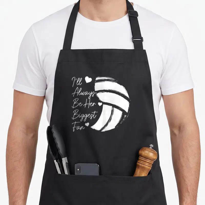 Volleyball mom daughter apron - White stacked text I'll Always Be Her Biggest Fan next to a large volleyball and three — shown on a black cotton canvas apron against a white background
