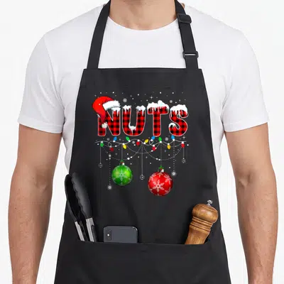 Chest nut family christmas aprons - NUTS text in buffalo plaid with Santa hat, snow, and hanging Christmas ornaments — shown on a black cotton canvas apron against a white background