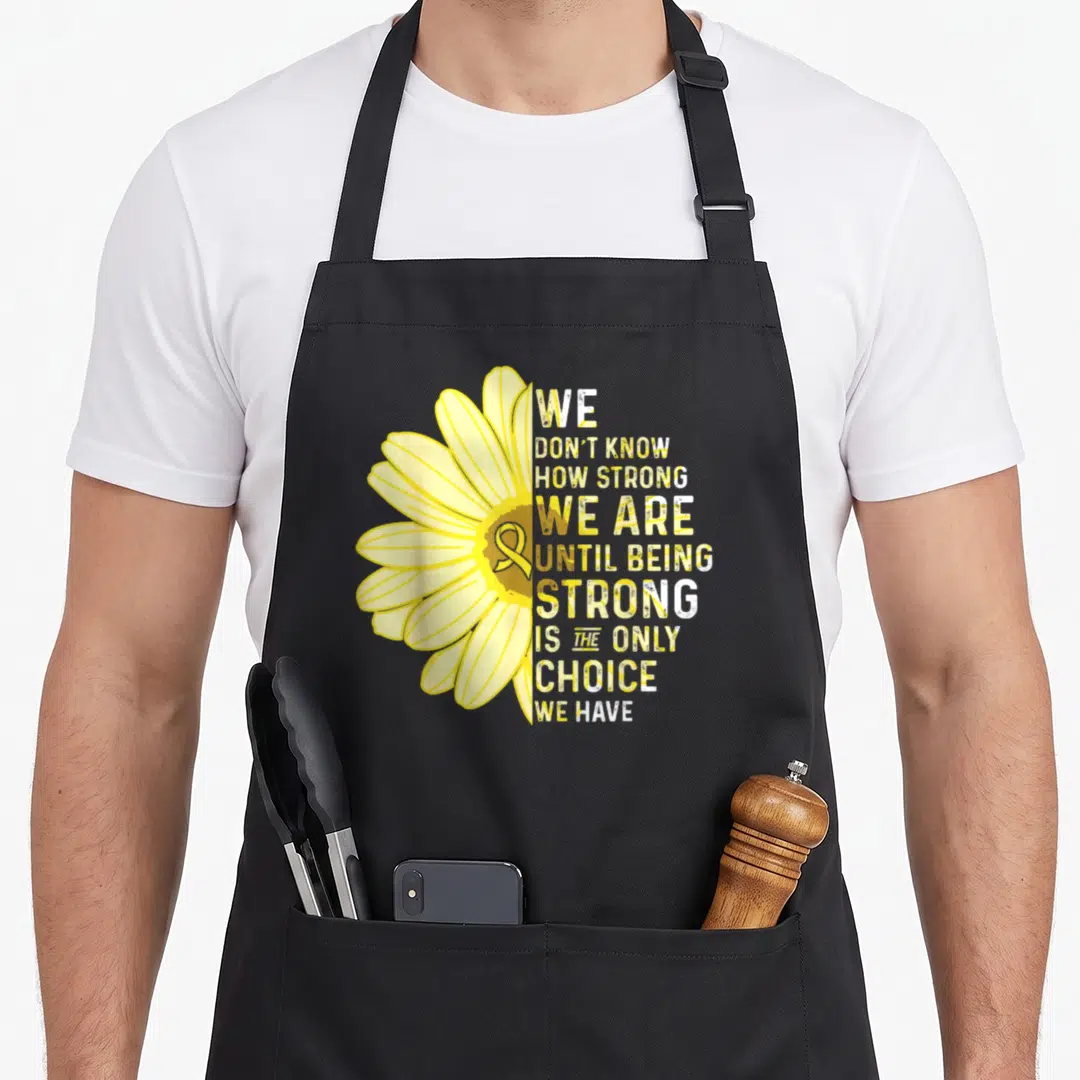 Strong sarcoma ribbon apron - Yellow flower with awareness ribbon center and stacked inspirational text block — shown on a black cotton canvas apron against a white background