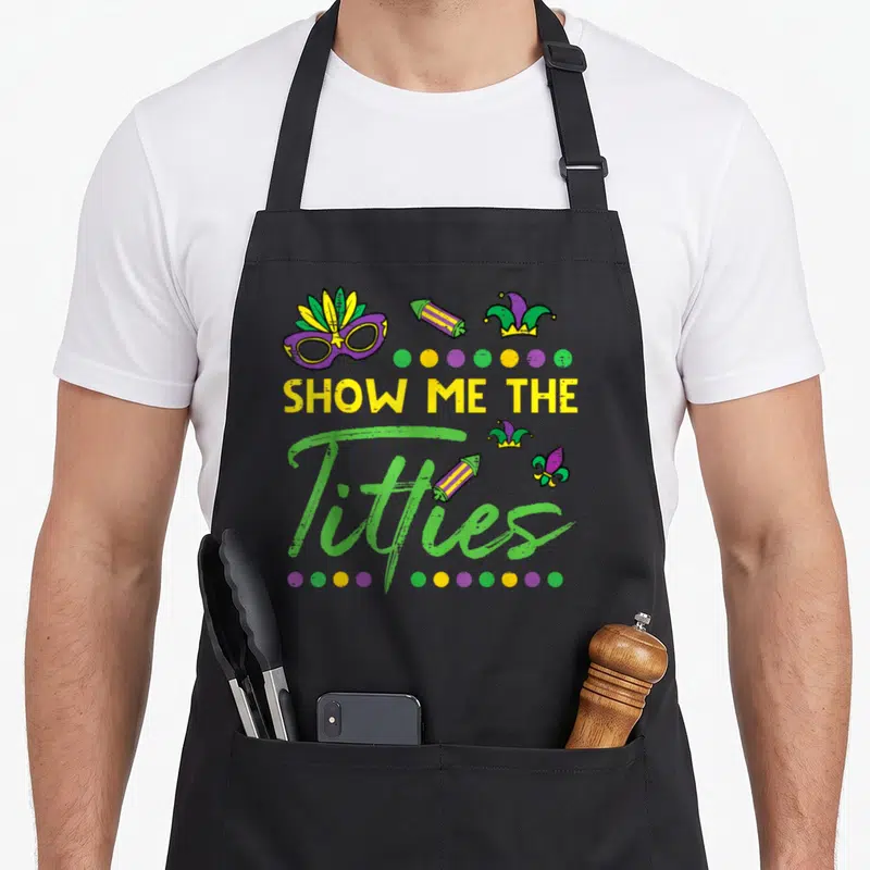 Show fat chef apron - SHOW ME THE Titties text with jester mask firecrackers and colored dots — shown on a black cotton canvas apron against a white background
