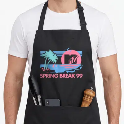 Mtv spring aprons - Retro pink and blue beach scene with MTV logo in sun, palm trees, and SPRING BREAK 99 text — shown on a black cotton canvas apron against a white background