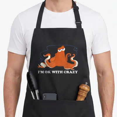 Finding crazy octopus man apron - Orange octopus with blue line and small fish, white text I'M OK WITH CRAZY below — shown on a black cotton canvas apron against a white background