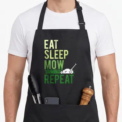 Eat grass cutting apron - Vertical Eat Sleep Mow Repeat text with white lawn mower and grass blades in distressed green — shown on a black cotton canvas apron against a white background