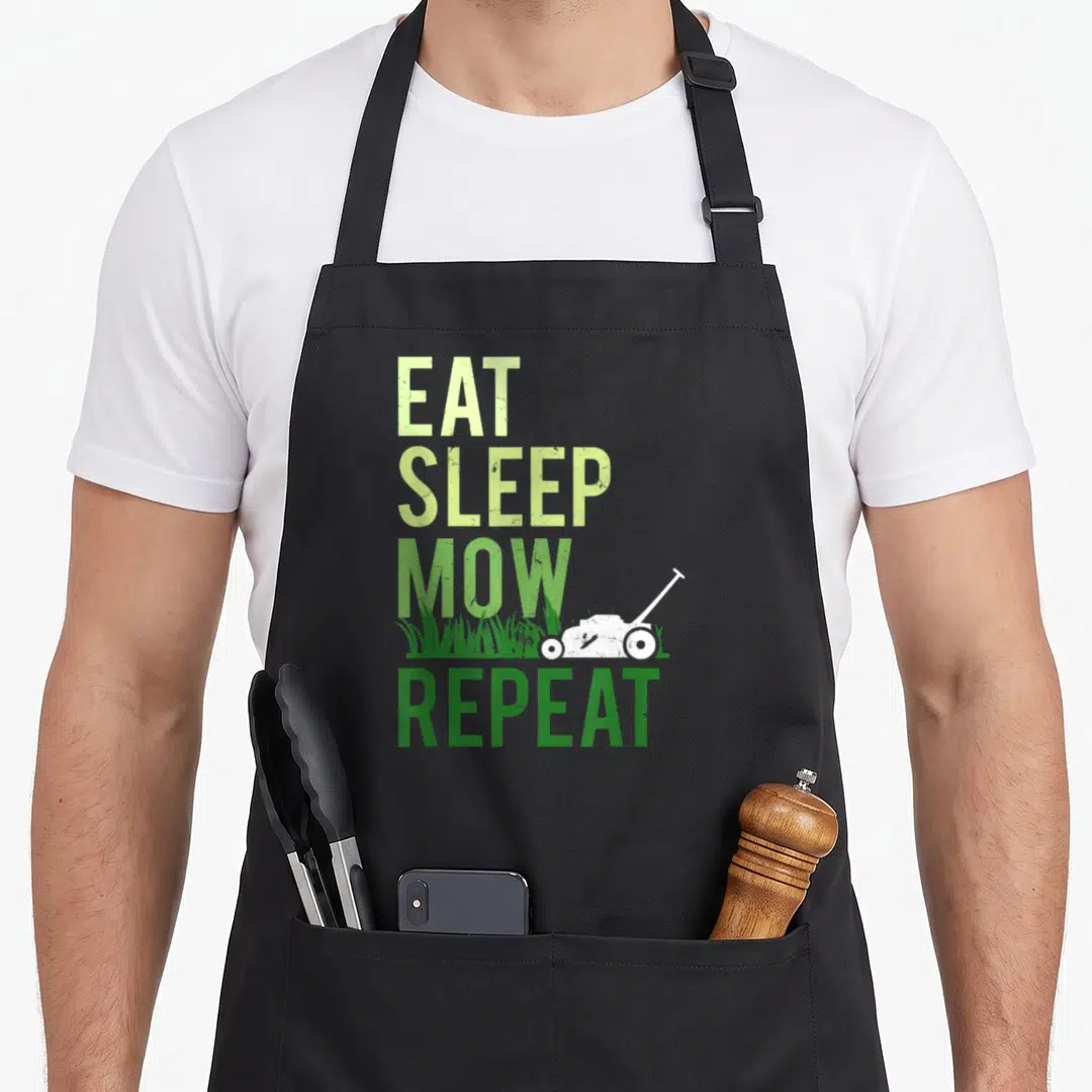 Eat grass cutting apron - Vertical Eat Sleep Mow Repeat text with white lawn mower and grass blades in distressed green — shown on a black cotton canvas apron against a white background
