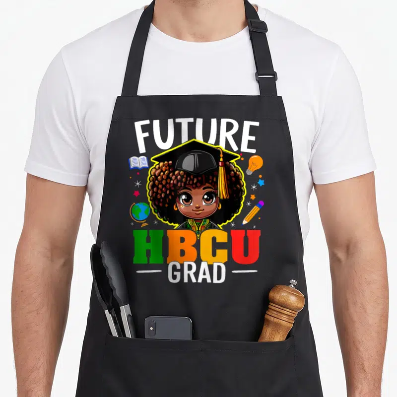 Grad future history apron - Cartoon girl in cap with FUTURE HBCU GRAD text and school supplies in yellow green orange — shown on a black cotton canvas apron against a white background
