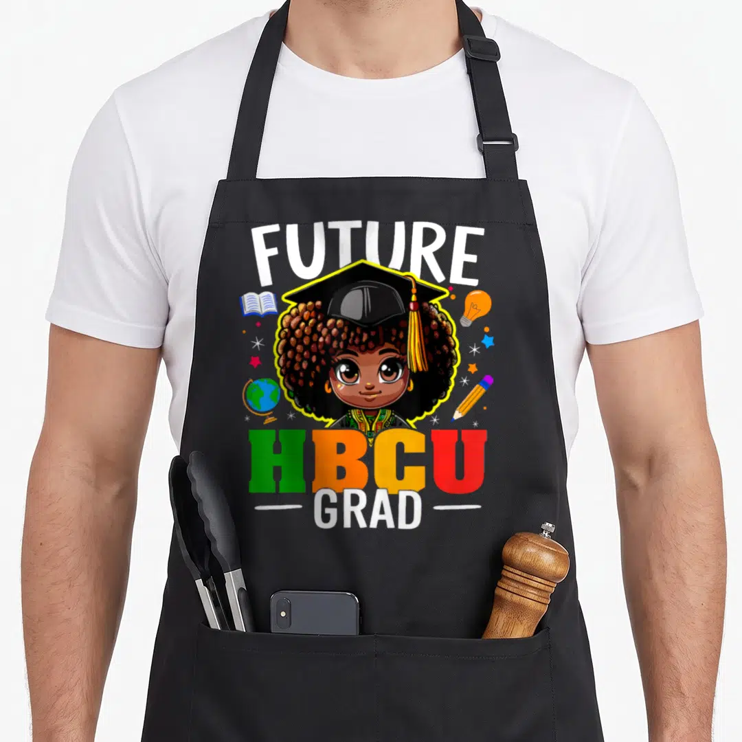 Grad future history apron - Cartoon girl in cap with FUTURE HBCU GRAD text and school supplies in yellow green orange — shown on a black cotton canvas apron against a white background