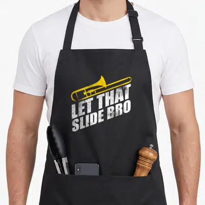 Slide skid apron - Yellow trombone above distressed white text LET THAT SLIDE BRO — shown on a black cotton canvas apron against a white background
