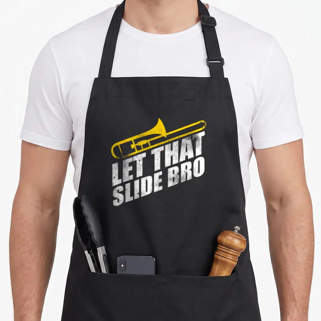 Slide skid apron - Yellow trombone above distressed white text LET THAT SLIDE BRO — shown on a black cotton canvas apron against a white background