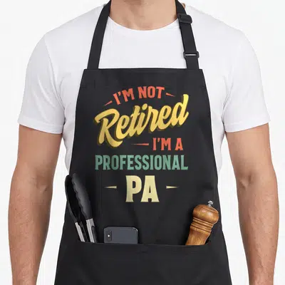Funny retired professional apron - Stacked colorful text reading I'M NOT Retired I'M A PROFESSIONAL PA with decorative — shown on a black cotton canvas apron against a white background
