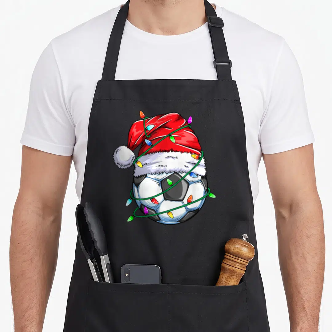 Soccer christmas santa apron - Cartoon soccer ball with red Santa hat and multicolored Christmas lights on black apron — shown on a black cotton canvas apron against a white background