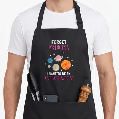 Vintage forget princess apron - Cartoon planets and stars with text FORGET PRINCESS I WANT TO BE AN ASTROPHYSICIST — shown on a black cotton canvas apron against a white background