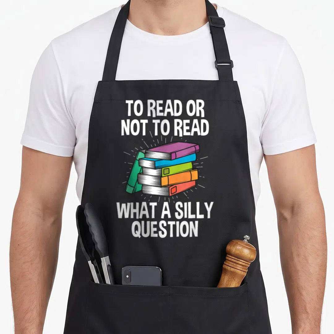 Read apron or apron - Four colorful books stacked with white rays and reading pun text in cartoon style — shown on a black cotton canvas apron against a white background