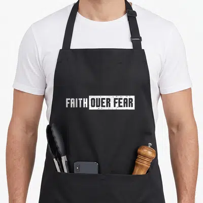 Fear catholic apron - FAITH OVER FEAR white distressed text inside rectangular box on black fabric — shown on a black cotton canvas apron against a white background