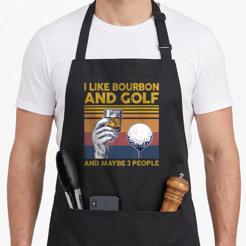 Bourbon golf apron - Retro graphic of hand holding glass next to golf ball on tee with yellow and blue striped — shown on a black cotton canvas apron against a white background