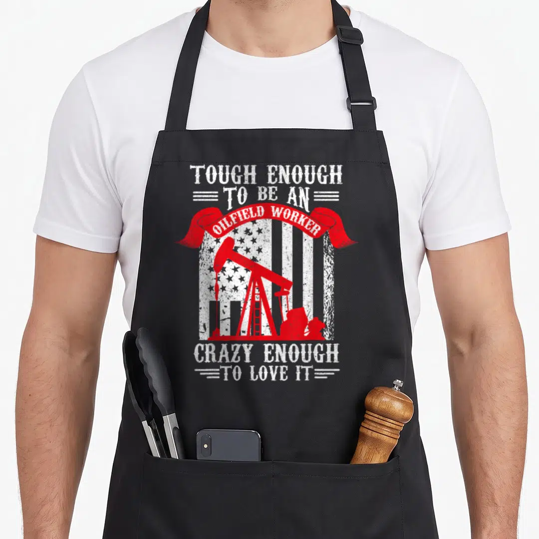 Oilfield oil mom apron - Red oil pump jack on distressed flag with white text TOUGH ENOUGH TO BE AN OILFIELD WORKER — shown on a black cotton canvas apron against a white background