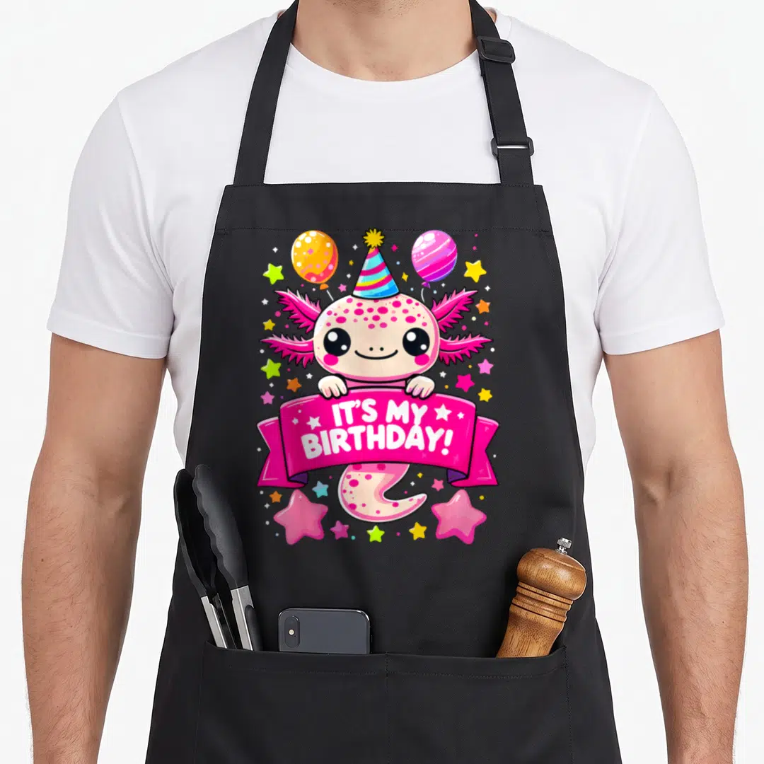Cute axolotl birthday apron - Pink axolotl holding IT'S MY BIRTHDAY! banner with party hat and balloons — shown on a black cotton canvas apron against a white background