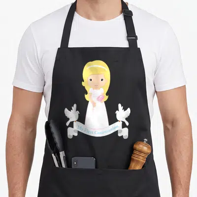 Daughter communion aprons - Cartoon girl holding pink bible and rosary flanked by two doves with My First Communion — shown on a black cotton canvas apron against a white background