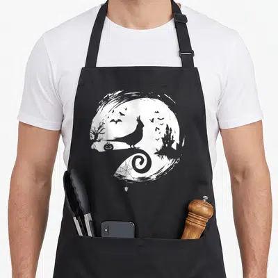 Cockatiel halloween apron - Grey cockatiel silhouette on white moon with bats, castle, pumpkin, and spider web — shown on a black cotton canvas apron against a white background