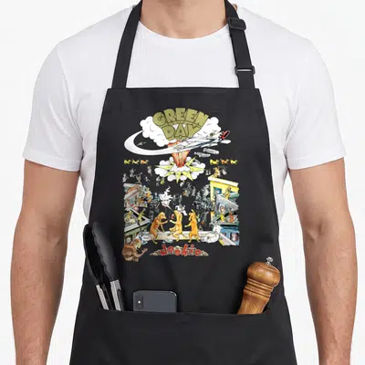 Dookie day comfort apron - Green Day Dookie cartoon city scene with rocket, dogs, and explosion in yellow, red, white — shown on a black cotton canvas apron against a white background