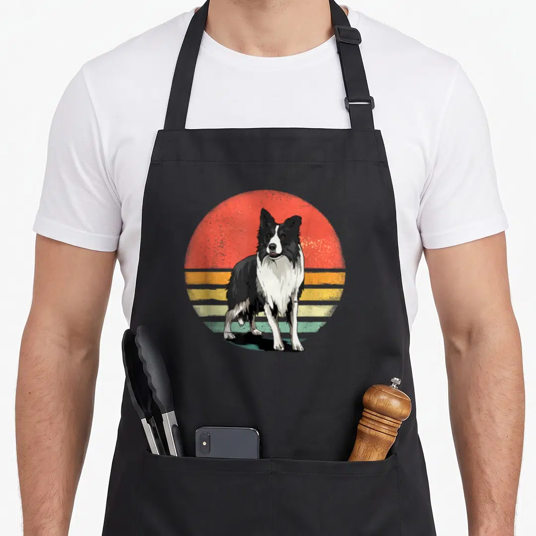 Pet border collie apron - Black and white dog standing in front of a red, yellow, and teal striped retro sun graphic — shown on a black cotton canvas apron against a white background