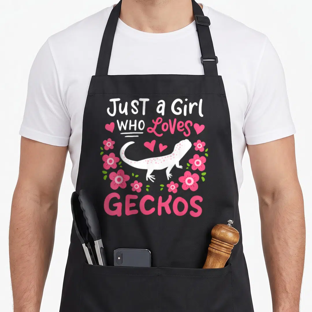 Funny gecko leopard apron - White cartoon gecko surrounded by pink flowers and hearts with text Just a Girl Who Loves — shown on a black cotton canvas apron against a white background