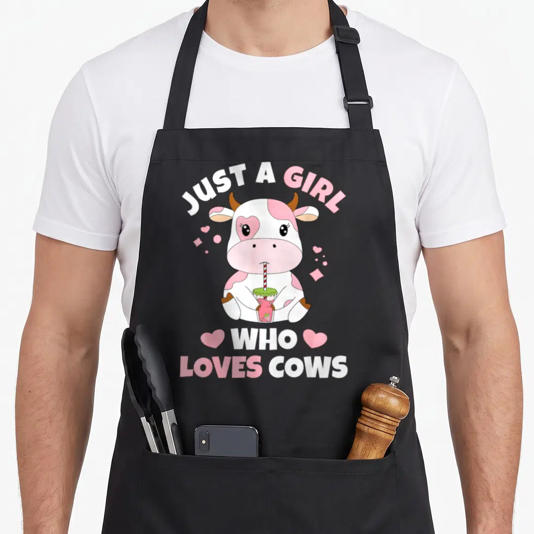 Cow strawberry apron - Cartoon cow holding strawberry drink with text Just A Girl Who Loves Cows and pink hearts — shown on a black cotton canvas apron against a white background