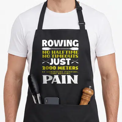 Halftime rowing apron - Stacked white and yellow text ROWING NO HALFTIME PAIN with horizontal and crossed oar graphics — shown on a black cotton canvas apron against a white background