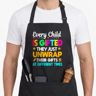 Gifted teacher apron - Every Child Is Gifted text with colorful dots, stars, pencil and paint palette — shown on a black cotton canvas apron against a white background