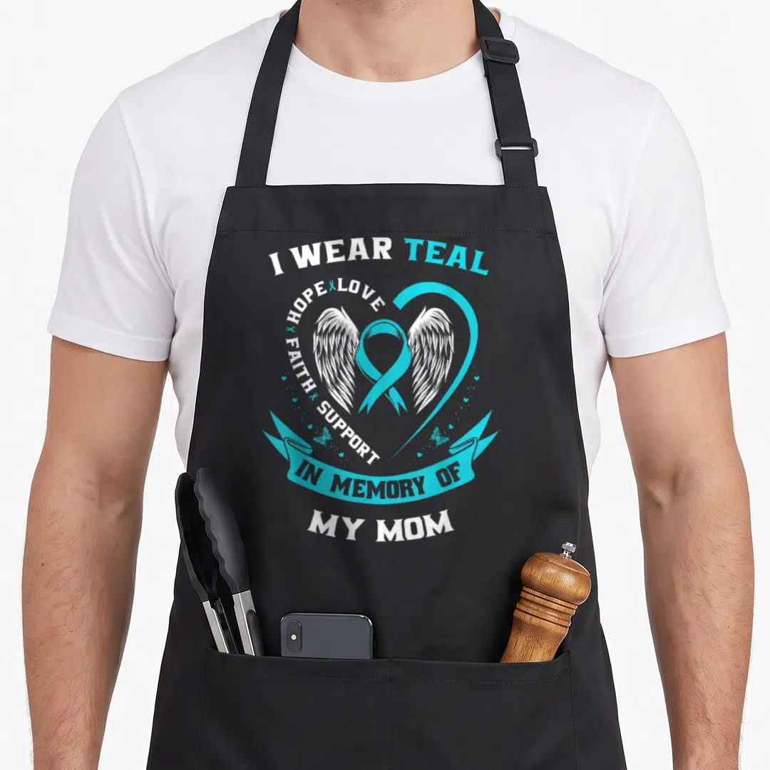 Vintage ovarian cancer awareness apron - Teal ribbon with white wings, heart outline, and In Memory Of My Mom text — shown on a black cotton canvas apron against a white background