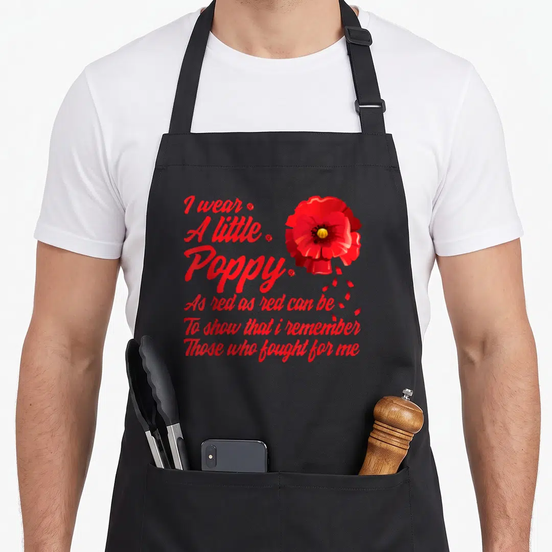 Poppy memorial apron - Red poppy with falling petals and stacked remembrance text on black background — shown on a black cotton canvas apron against a white background