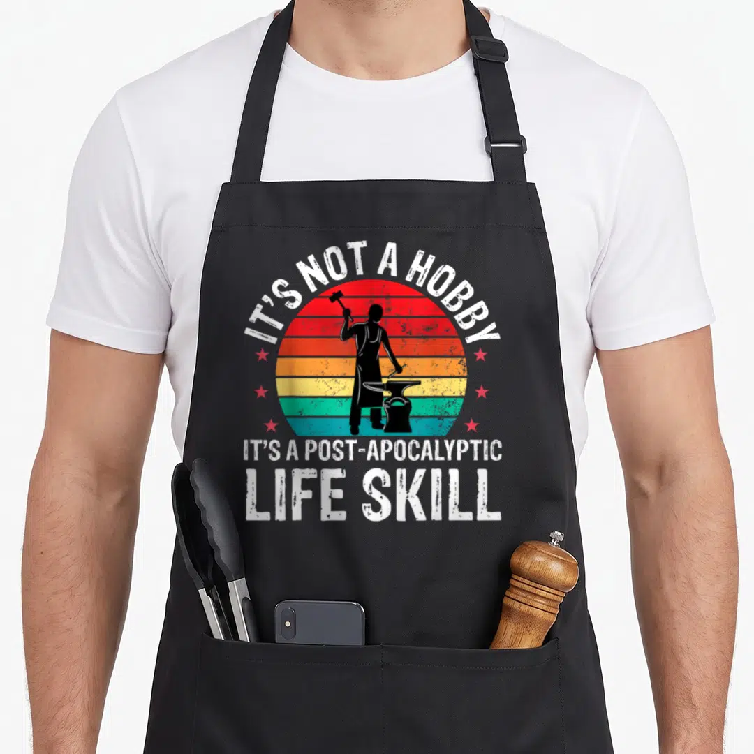 Anvil blacksmith apron - Blacksmith silhouette on striped sun with IT'S NOT A HOBBY text — shown on a black cotton canvas apron against a white background