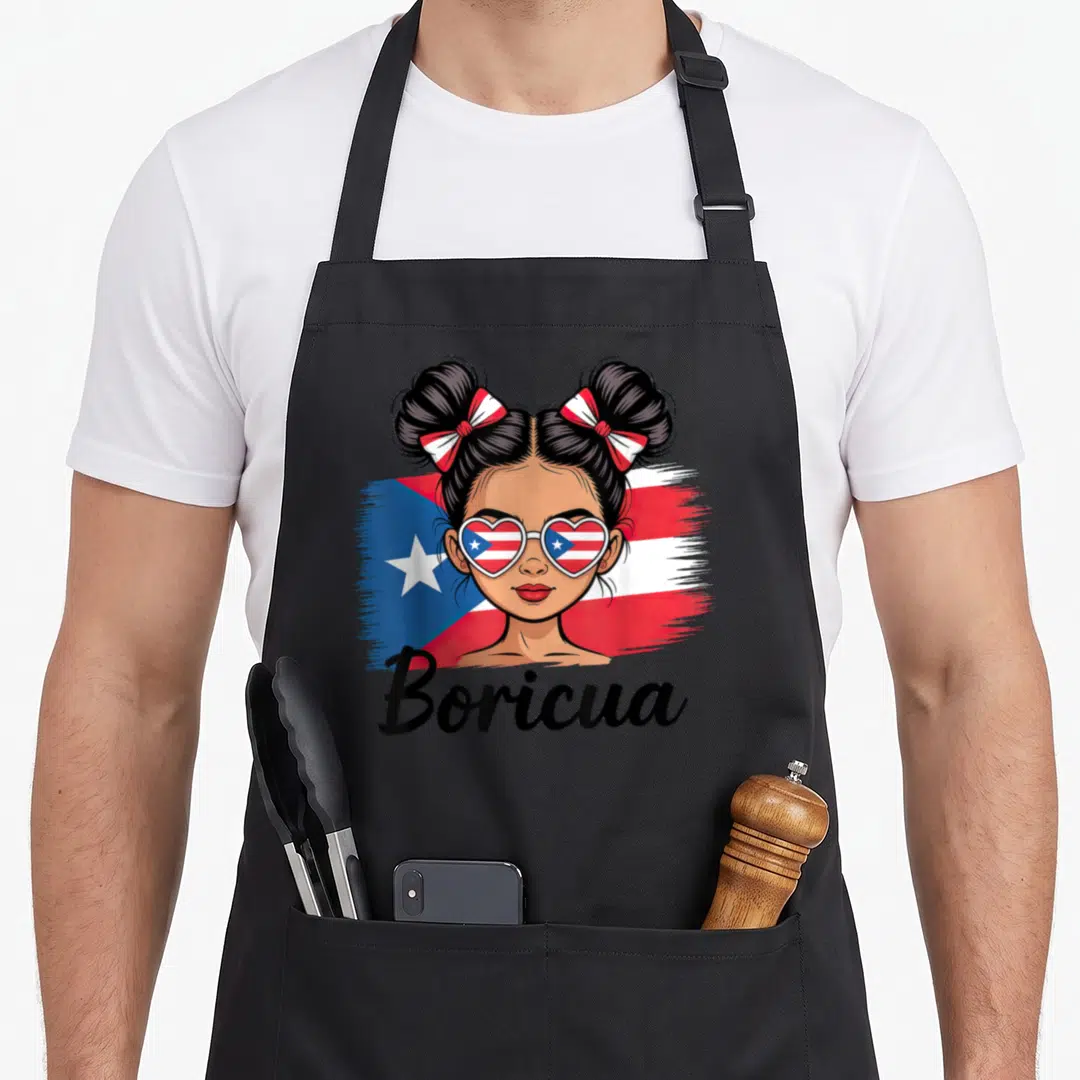 Hispanic messy aprons - Cartoon woman with double buns, heart sunglasses, and Boricua text over red white blue flag — shown on a black cotton canvas apron against a white background