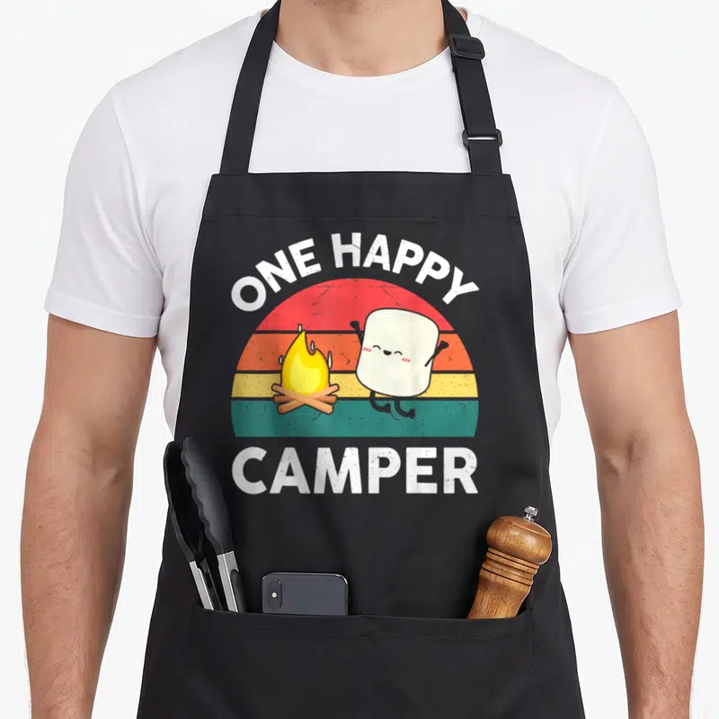 Camper toddler camping apron - ONE HAPPY CAMPER text over striped sun with jumping marshmallow and campfire — shown on a black cotton canvas apron against a white background