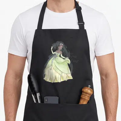 Follow princess apron - Watercolor princess in green gown with follow your heart script text — shown on a black cotton canvas apron against a white background