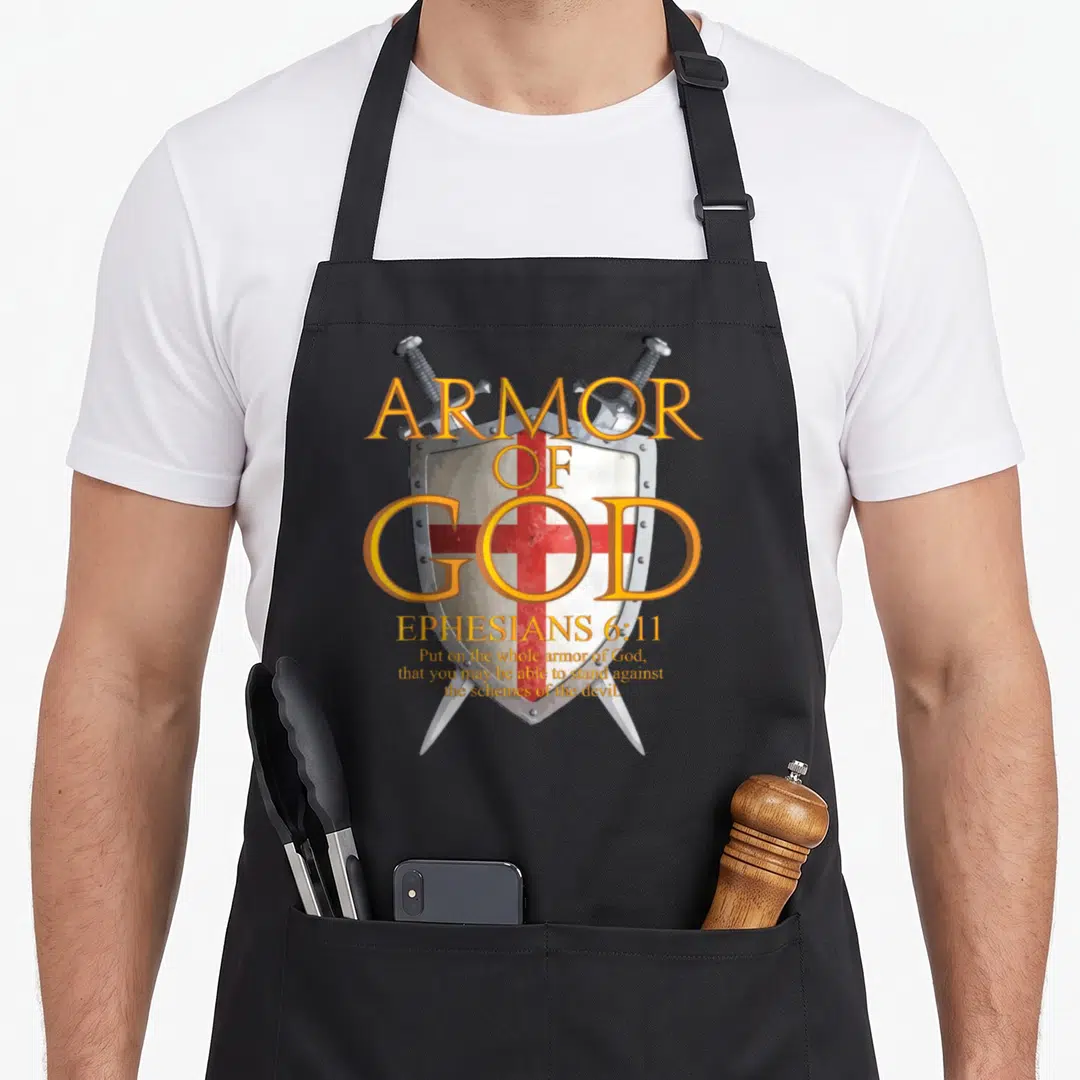 God ephesian bible verse apron - Shield with red cross, two crossed swords, and yellow-orange Armor of God text — shown on a black cotton canvas apron against a white background