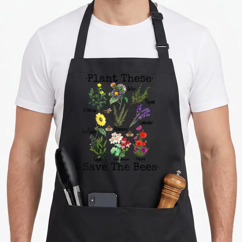 Save plant apron - Plant These and Save The Bees text with labeled flowers and three flying bees — shown on a black cotton canvas apron against a white background